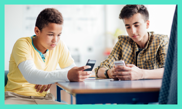 Two children sat at desk using mobile devices